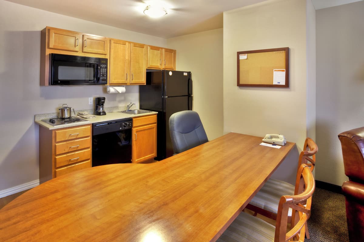 Una cocina compacta con armarios de madera, microondas, refrigerador y una mesa de comedor con sillas.