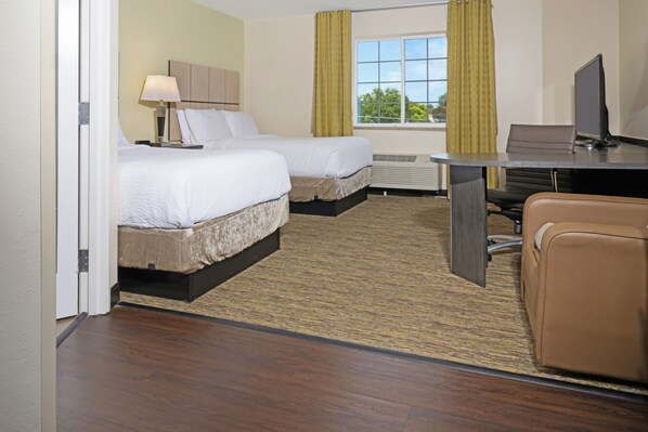 Quarto de hotel com duas camas, uma mesa, uma cadeira, uma televisão e uma janela com cortinas.