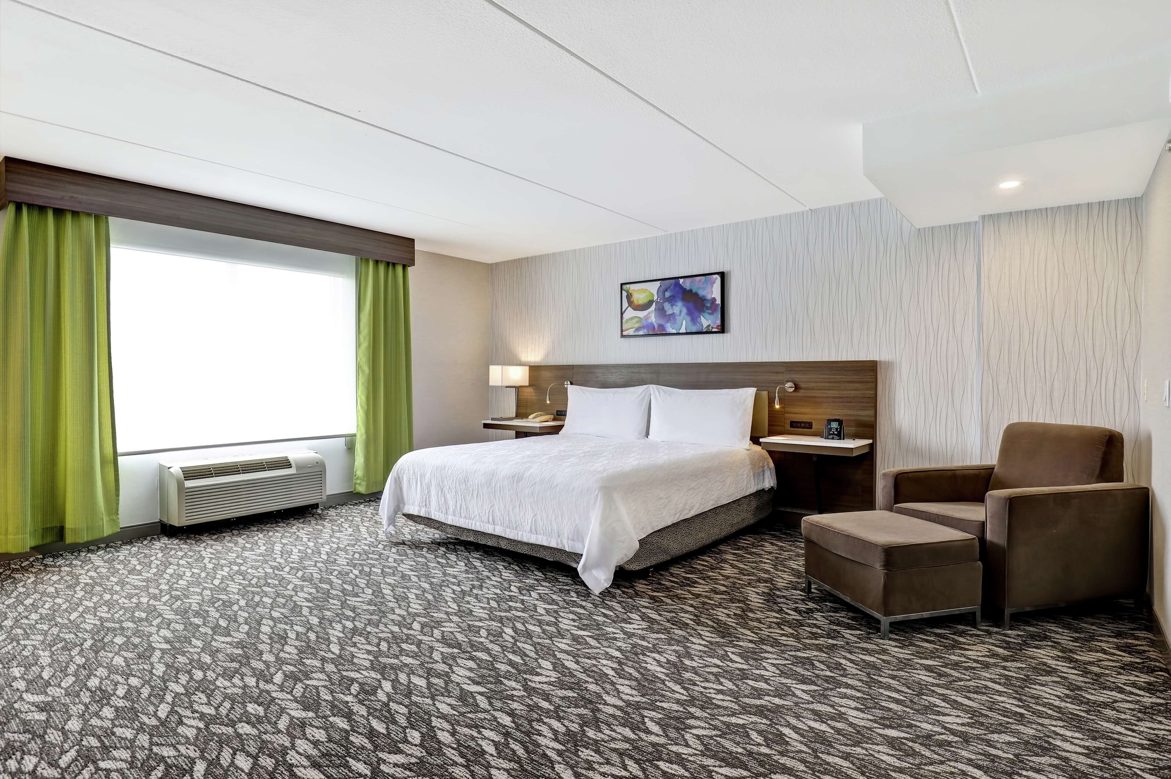 A hotel room with a large bed, a chair, a desk, and a window with curtains.