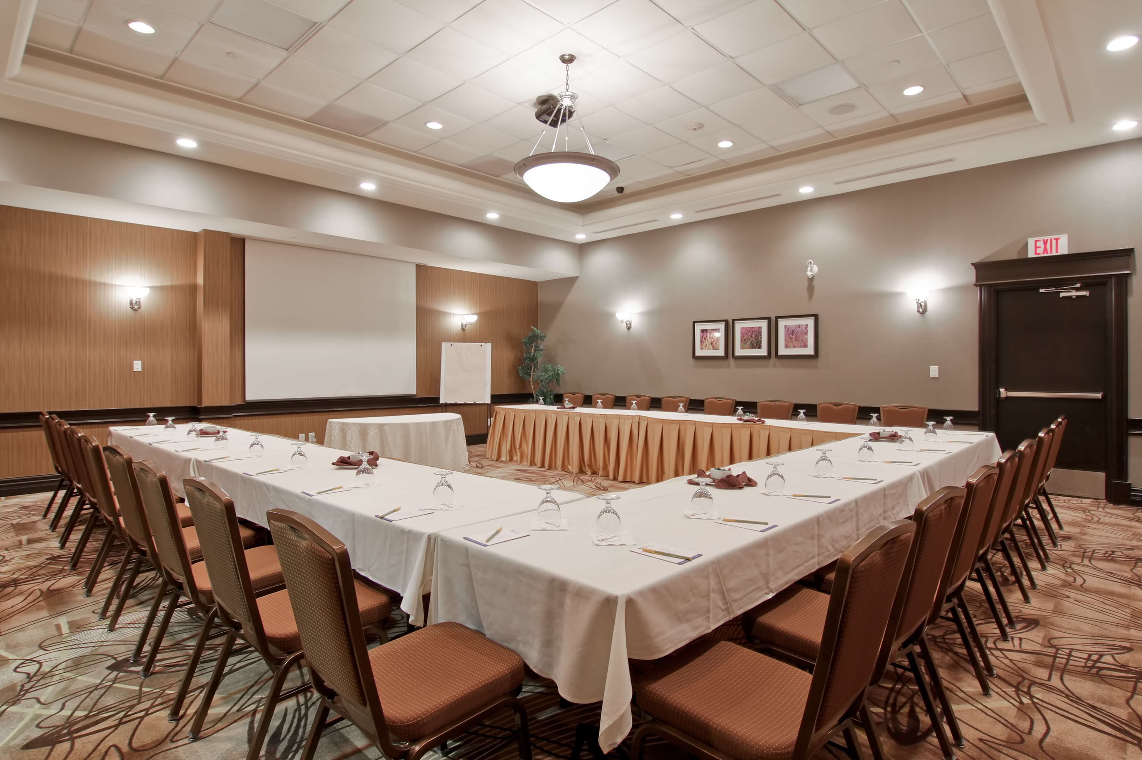 Un salón de conferencias con una larga mesa, sillas, una pantalla de proyector y una señal de salida.