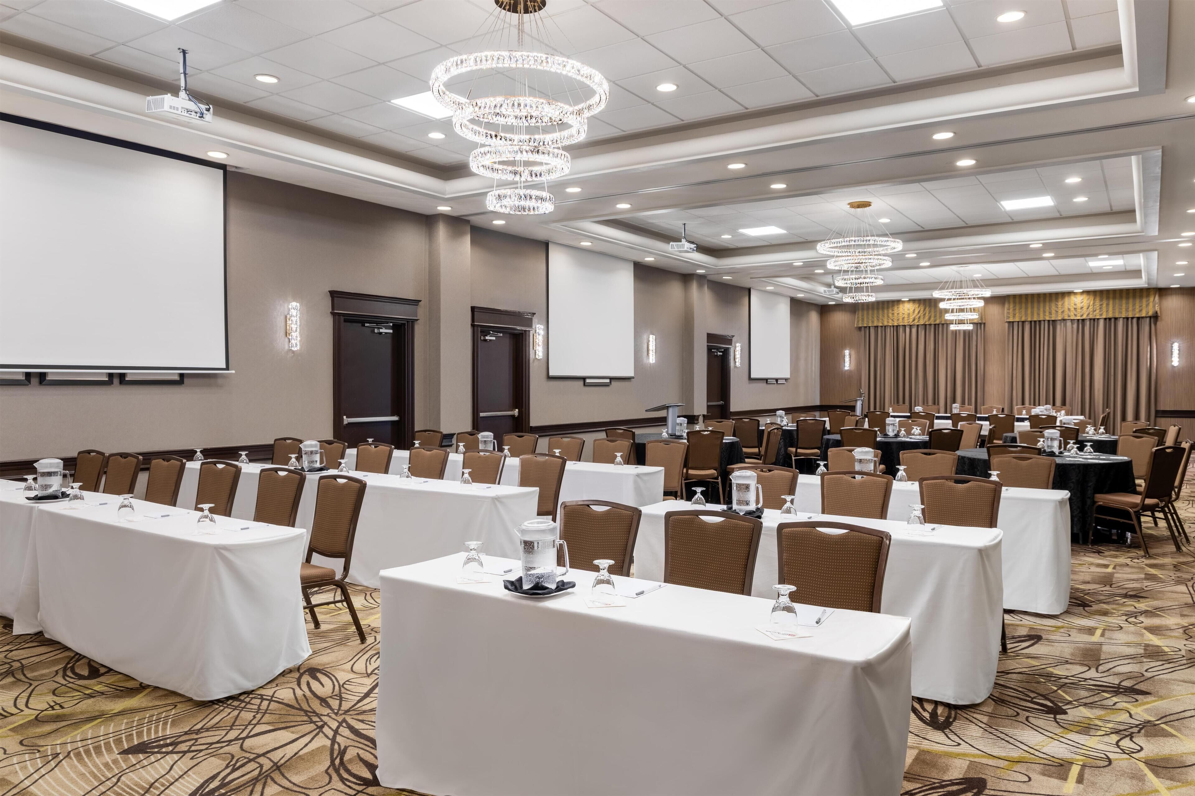 A conference room with multiple tables, chairs, a projector screen, and a large screen.