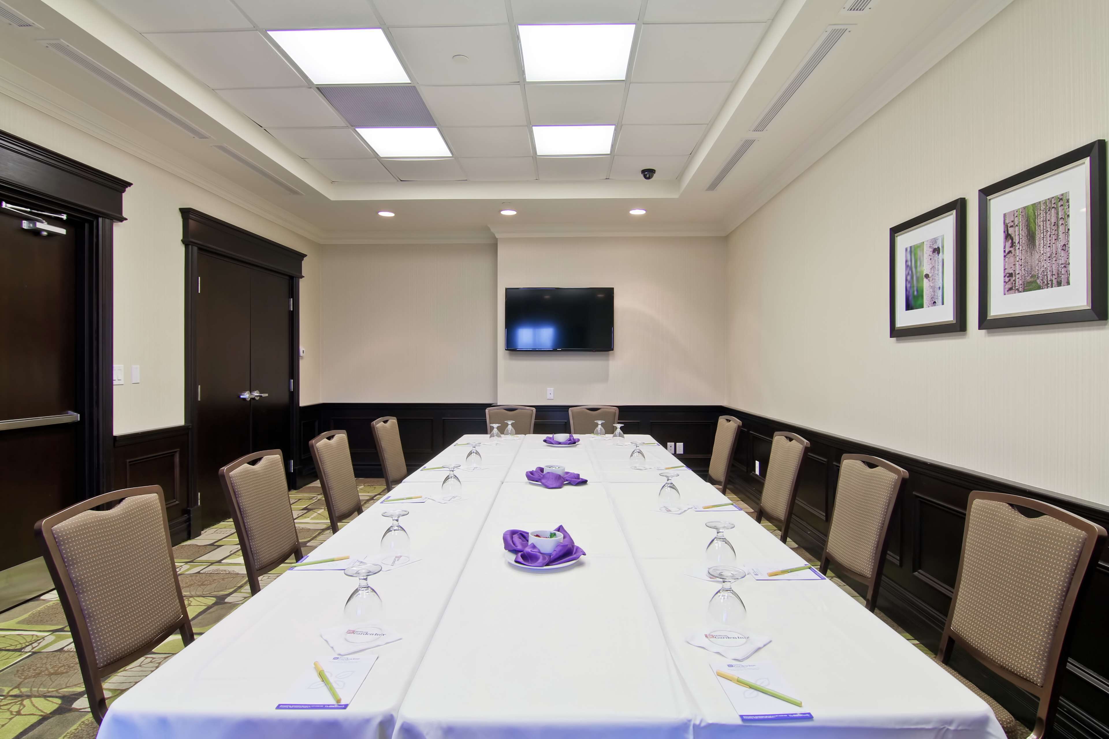 Un salón de conferencias con una larga mesa, sillas, un televisor y cuadros en la pared.