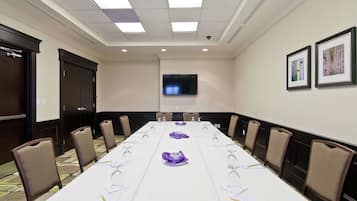 Un salón de conferencias con una larga mesa, sillas, un televisor y cuadros en la pared.