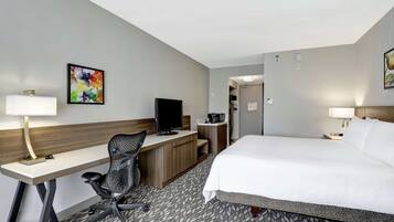 Una habitación de hotel con cama, escritorio, silla, televisor y obras de arte en las paredes.