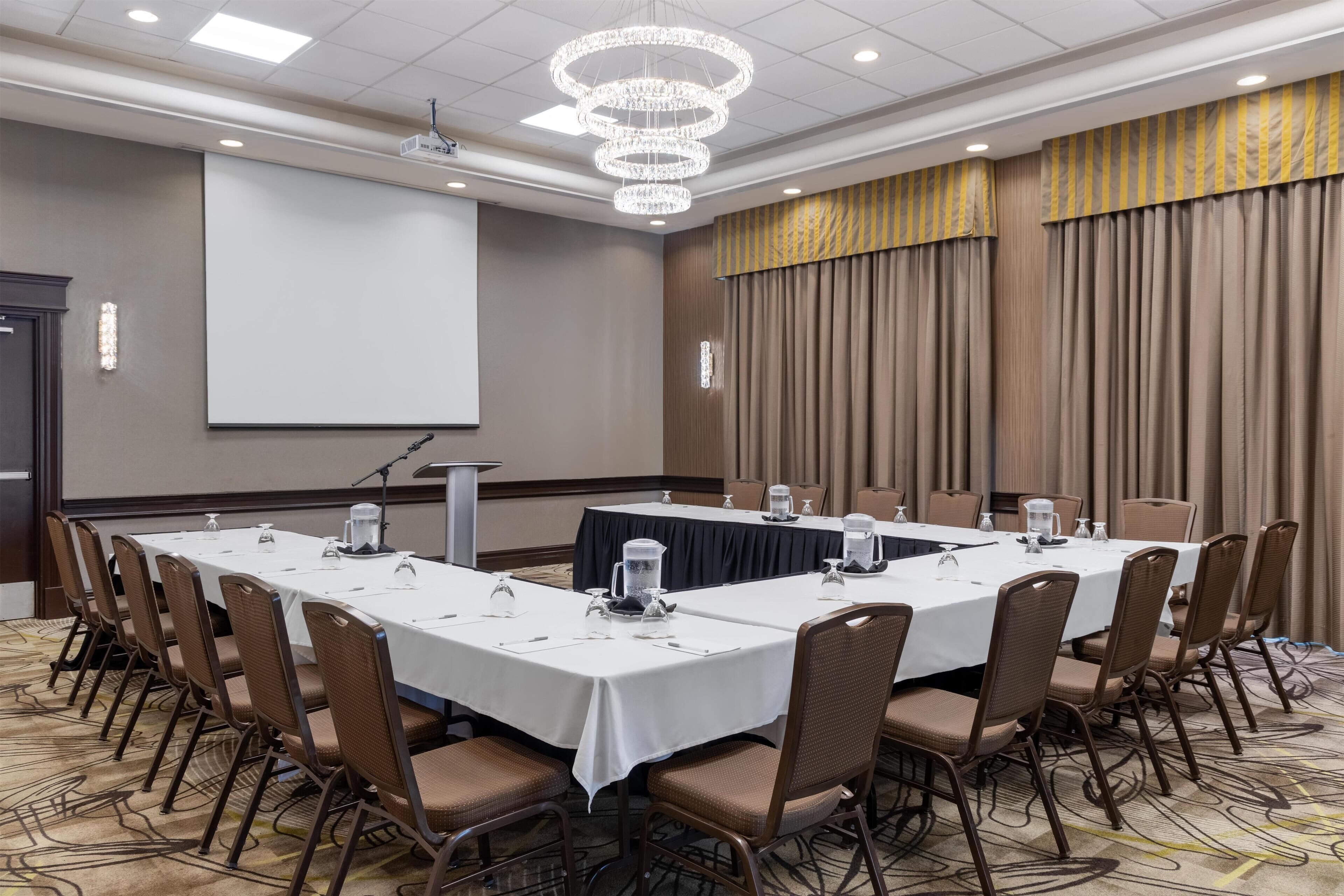A conference room with a long table, chairs, a projector screen, and a chandelier.