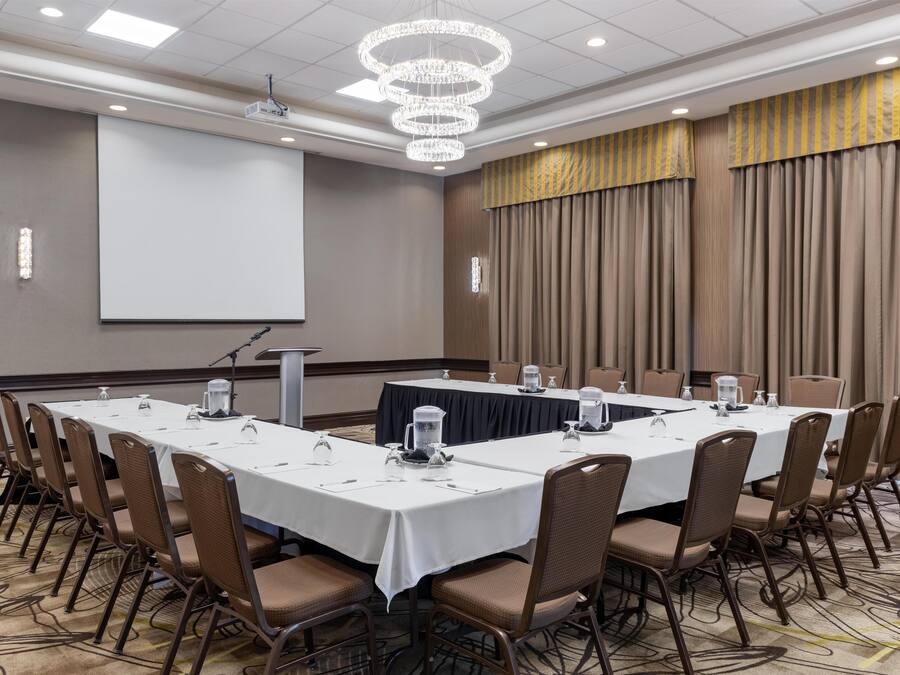 A conference room with a long table, chairs, a projector screen, and a chandelier.