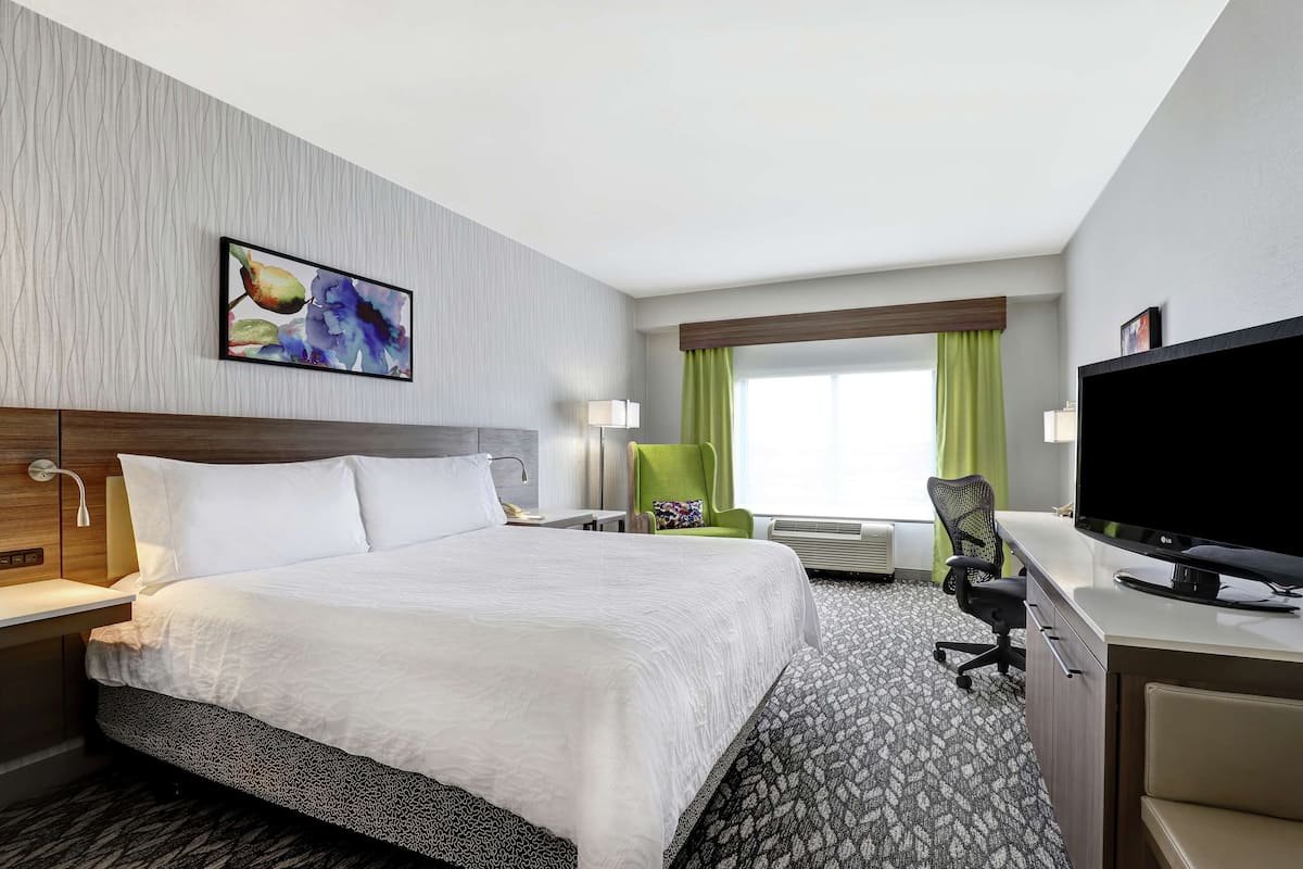 A hotel room with a large bed, a desk with a computer, a TV, and a window with curtains.