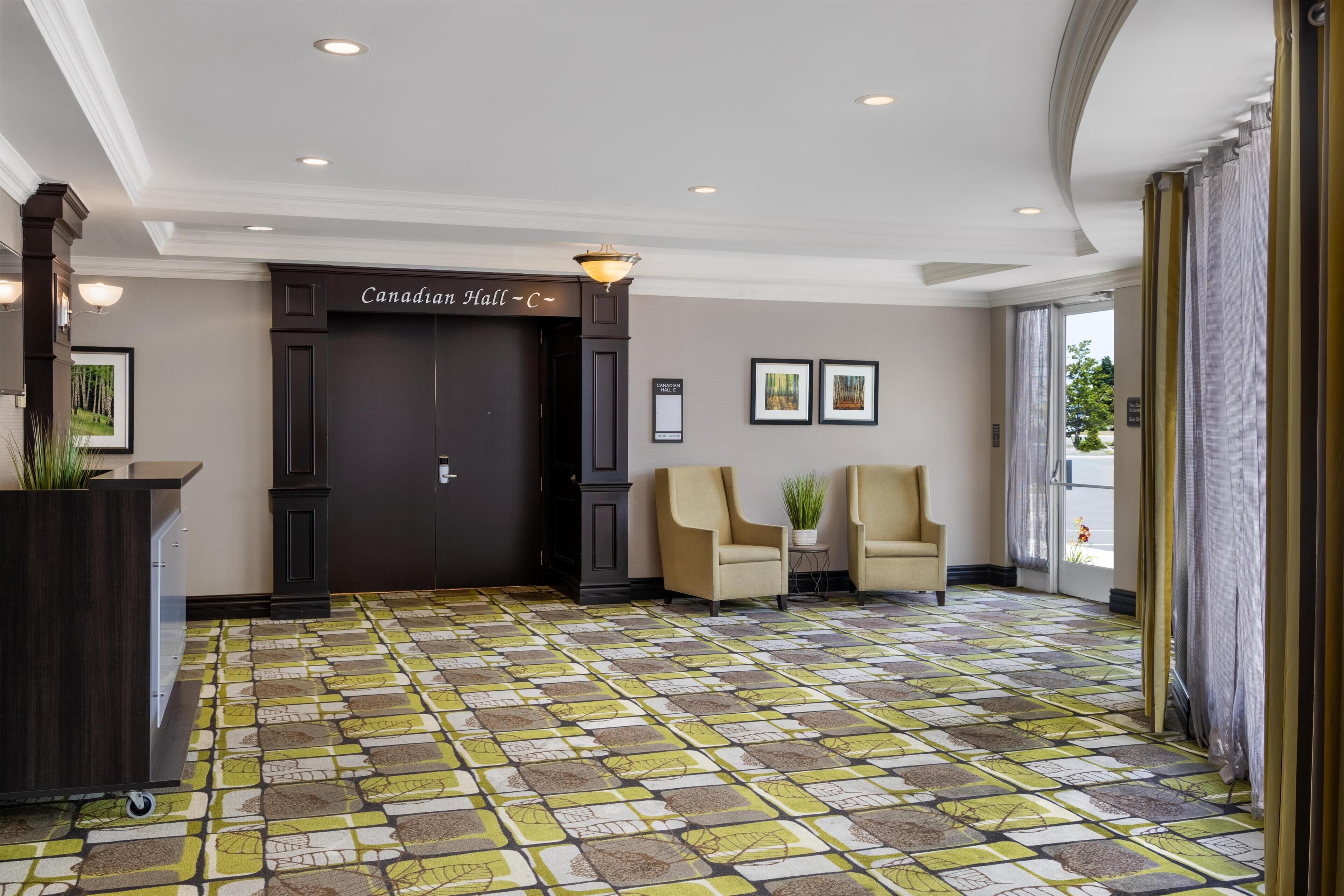 Un vestíbulo con mostrador de recepción, dos sillones, una puerta con la inscripción "Canadian Hall" y un suelo estampado.