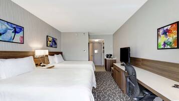 Une chambre d’hôtel avec deux lits, un bureau, une chaise, une télévision et des œuvres d’art accrochées aux murs.