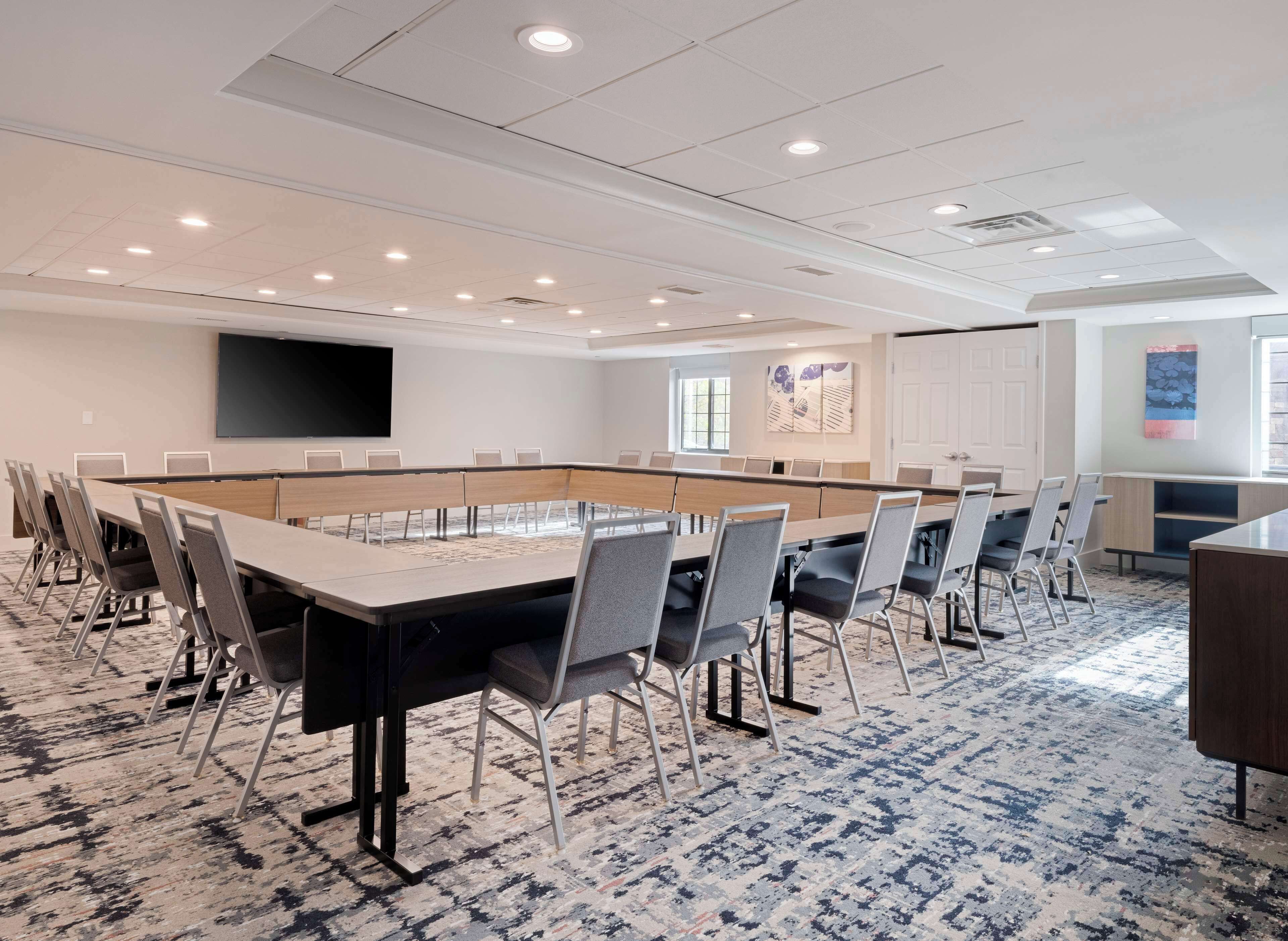 A conference room with a long table, chairs, a projector screen, and a carpeted floor.
