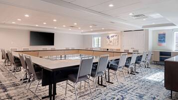 A conference room with a long table, chairs, a projector screen, and a carpeted floor.