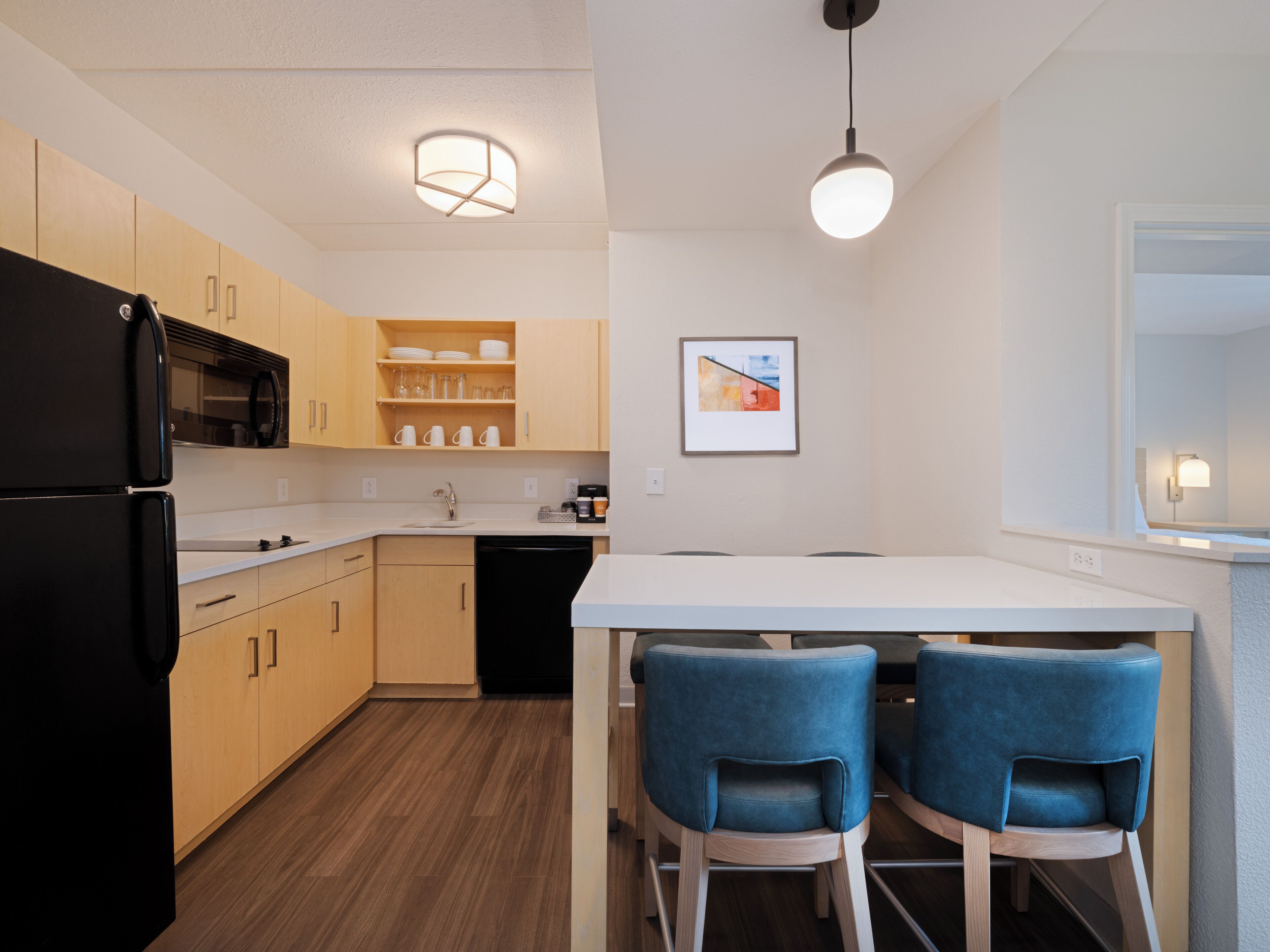 A modern kitchen with wooden cabinets, a black refrigerator, a white countertop, and two blue chairs.
