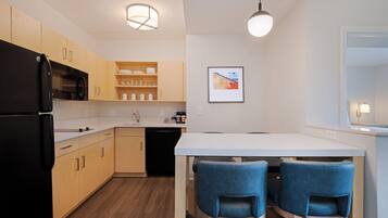 A modern kitchen with wooden cabinets, a black refrigerator, a white countertop, and two blue chairs.