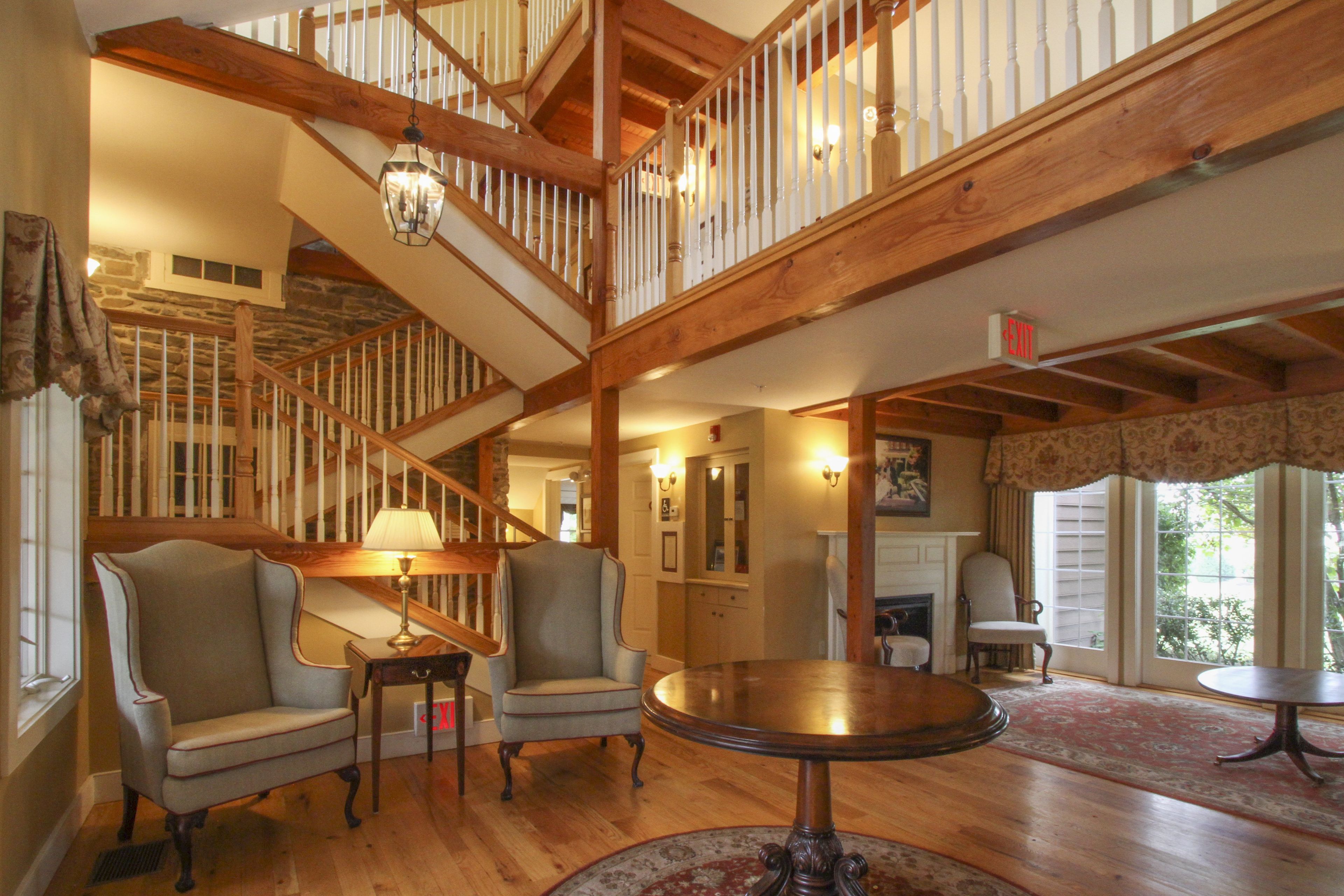 A multi-level wooden staircase with a chandelier, two armchairs, a round table, and a fireplace.
