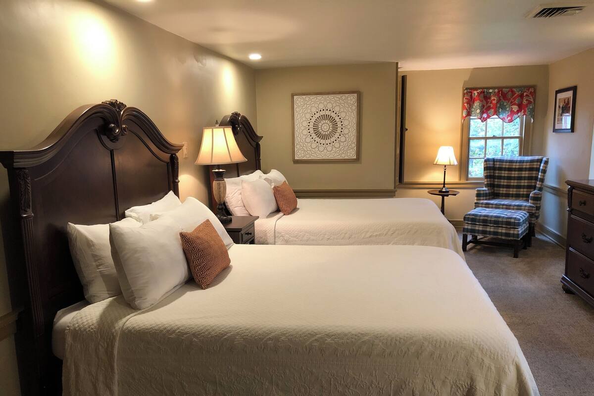 Ein Hotelzimmer mit zwei Betten, einem Sessel, einem Schminktisch und einem Fenster mit Blick.
