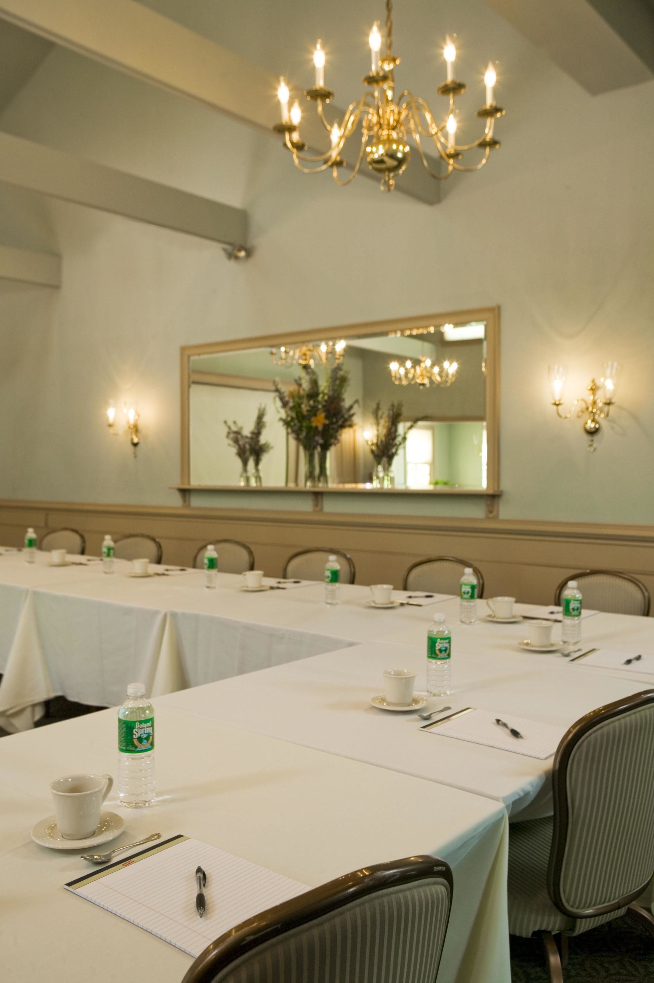 Uma sala de conferências com uma mesa comprida, cadeiras, um candelabro, um espelho e arandelas.