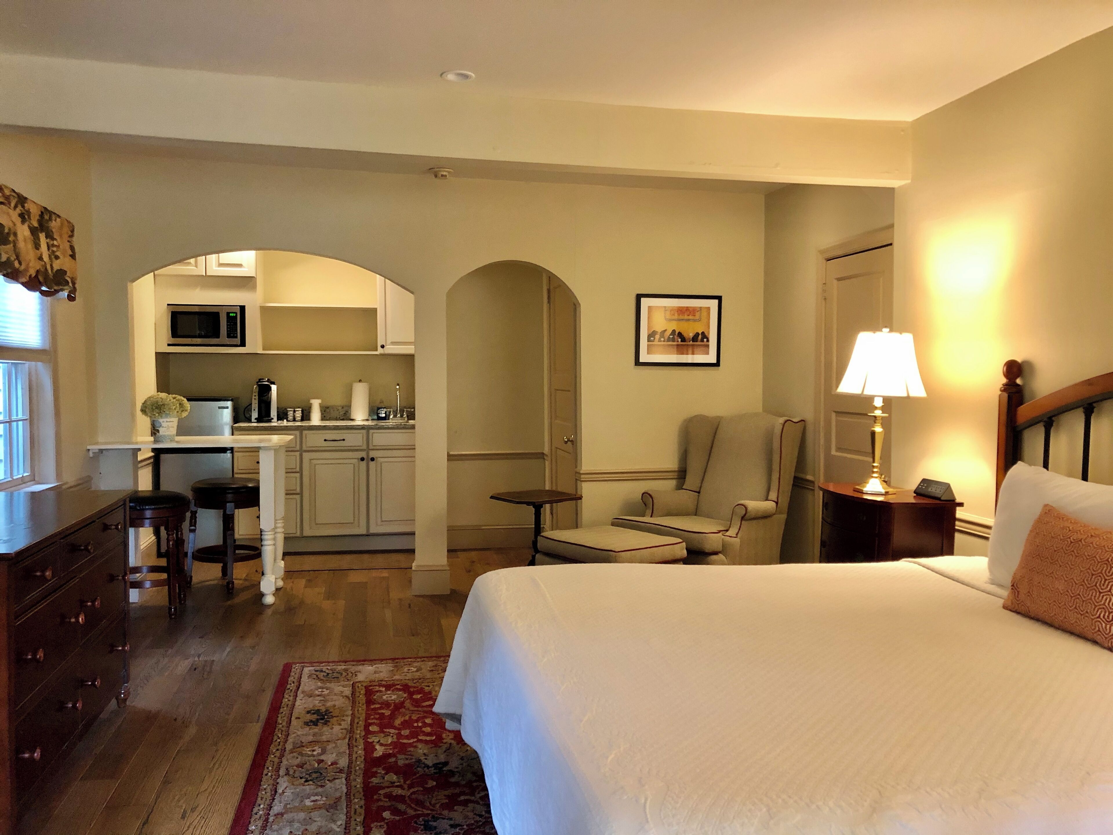 Habitación de hotel con cama, escritorio, silla, mesita, microondas, lavabo y armario.