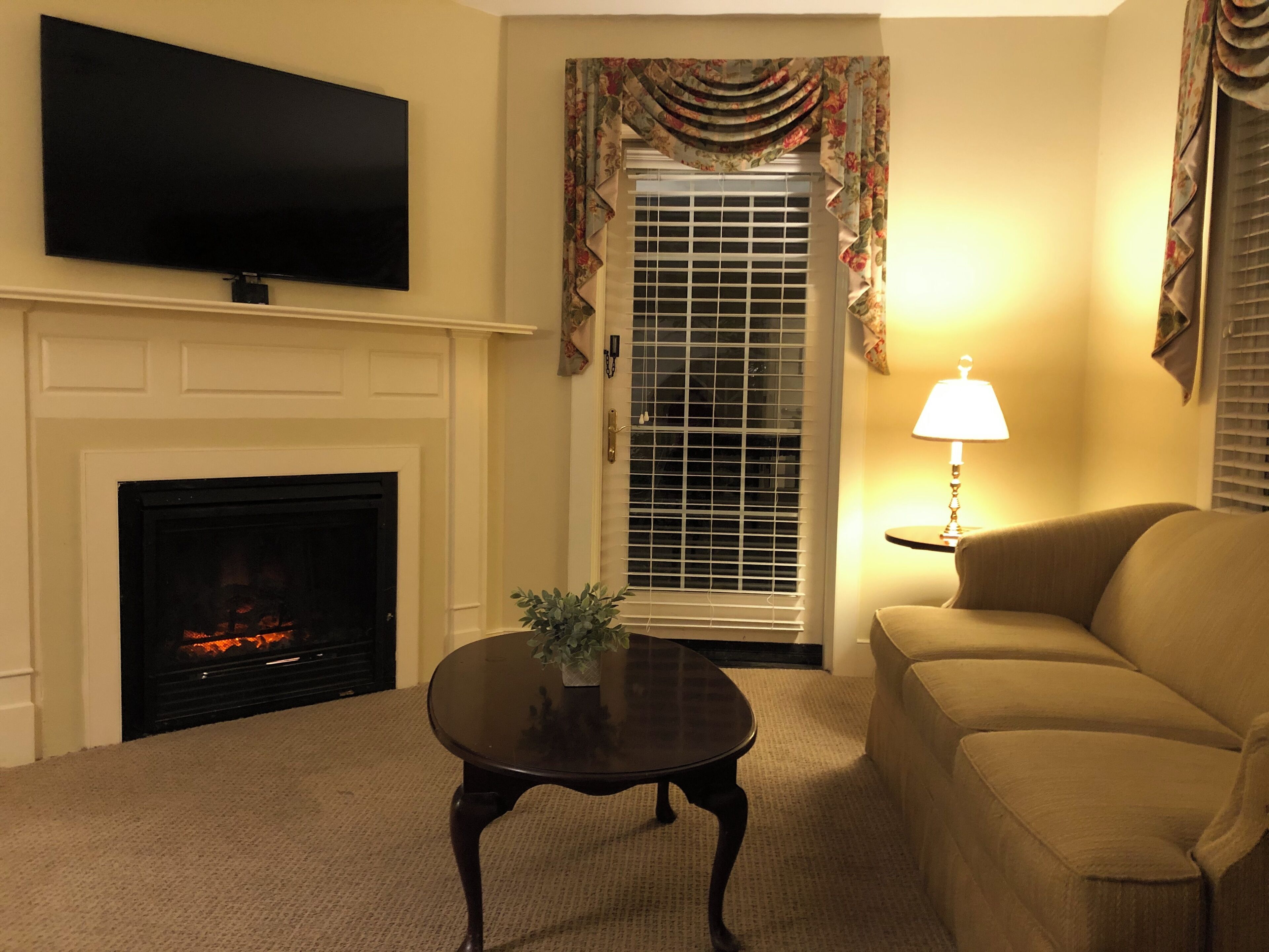 A living room with a fireplace, a television mounted on the wall, a sofa, and a lamp on a side table.