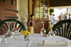 A dining table with clear glassware and a small vase of yellow flowers, set in a room with wooden chairs and a rustic ambiance.