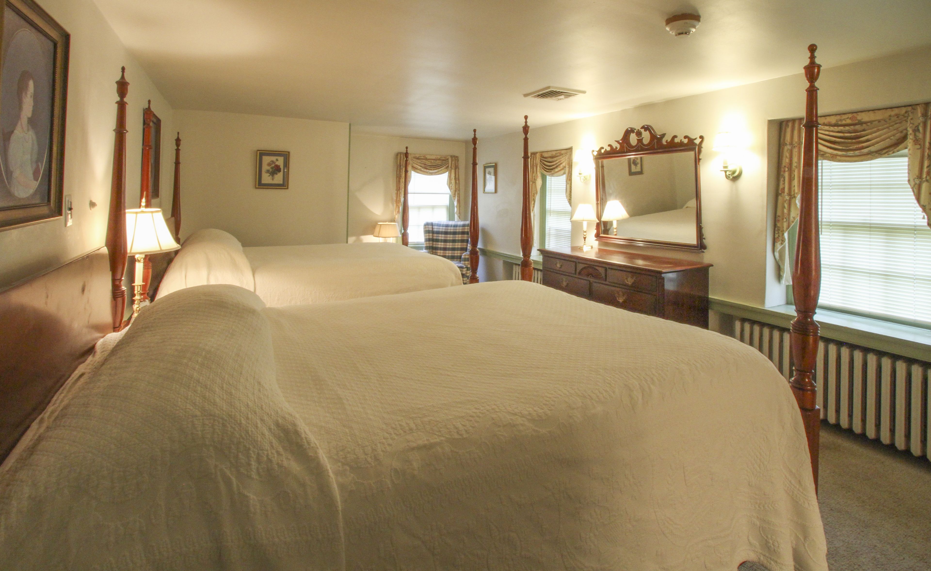 A hotel room with two beds, a dresser, a mirror, and a window with curtains.