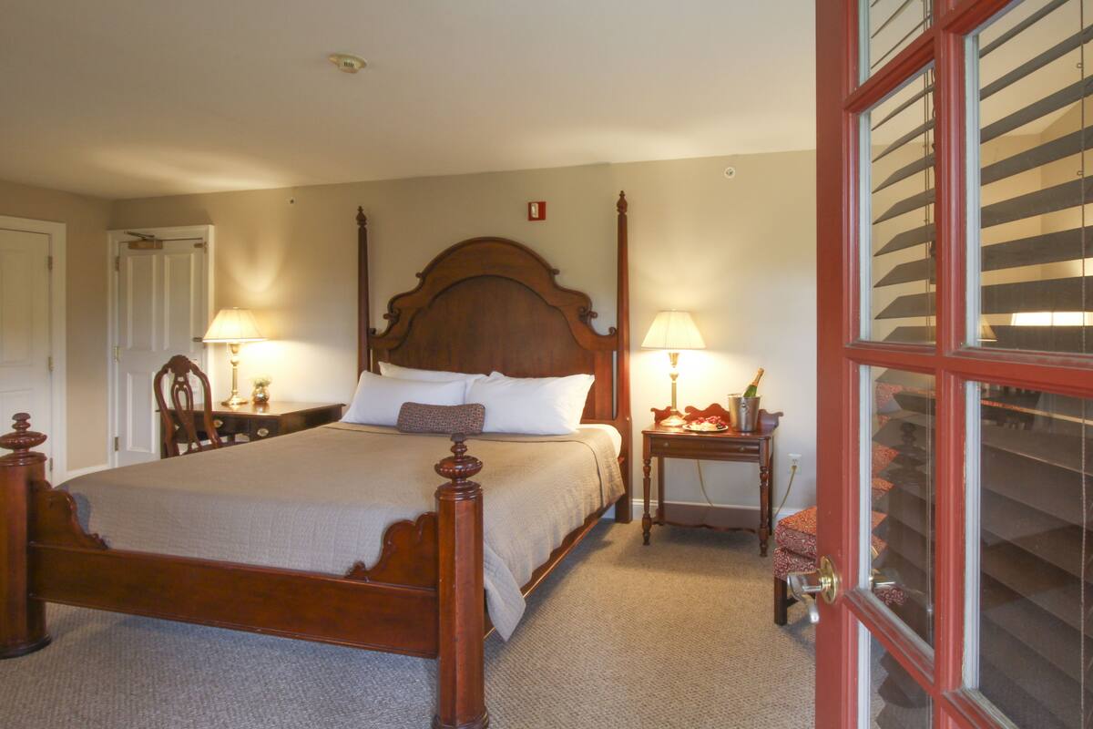 Ein traditionell eingerichtetes Schlafzimmer mit einem hölzernen Himmelbett, zwei Nachttischen mit Lampen und einem fensterartigen Element mit rotem Rahmen.