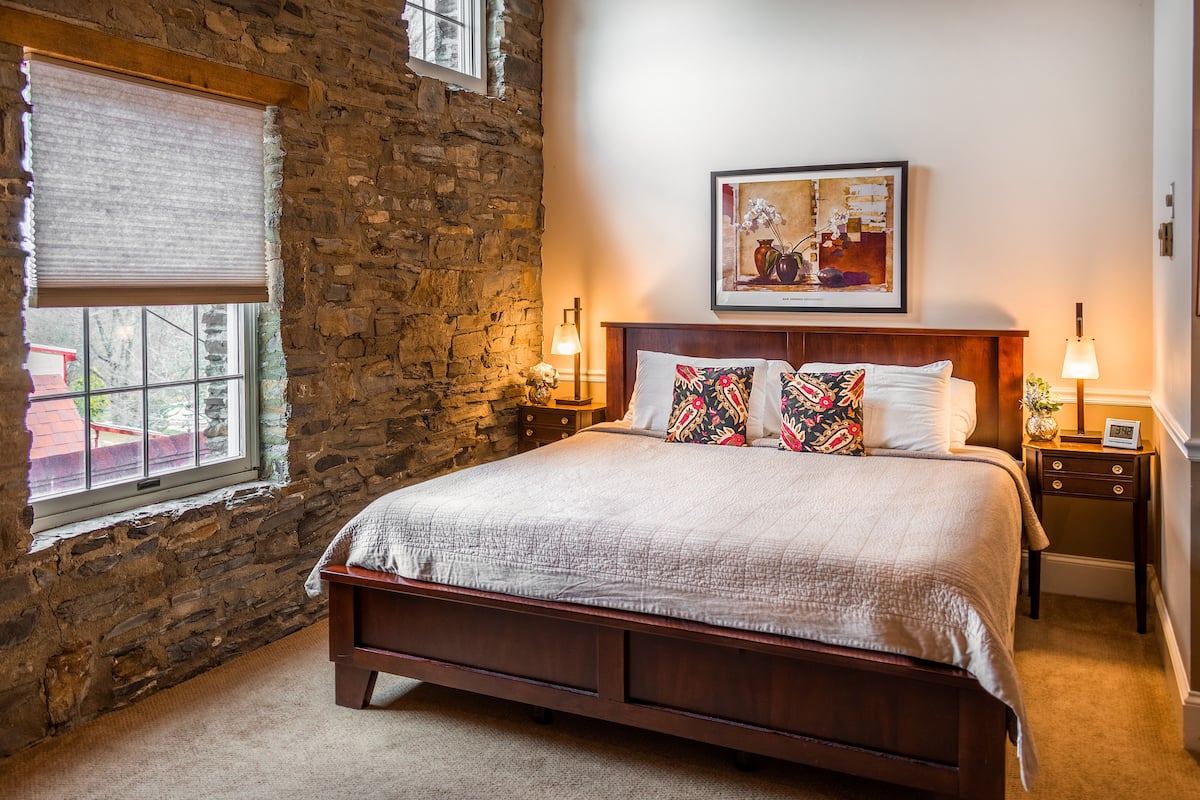 Ein Schlafzimmer mit Steinwand, einem großen Bett mit Steppdecke, zwei Nachttischlampen und einem gerahmten Bild an der Wand.