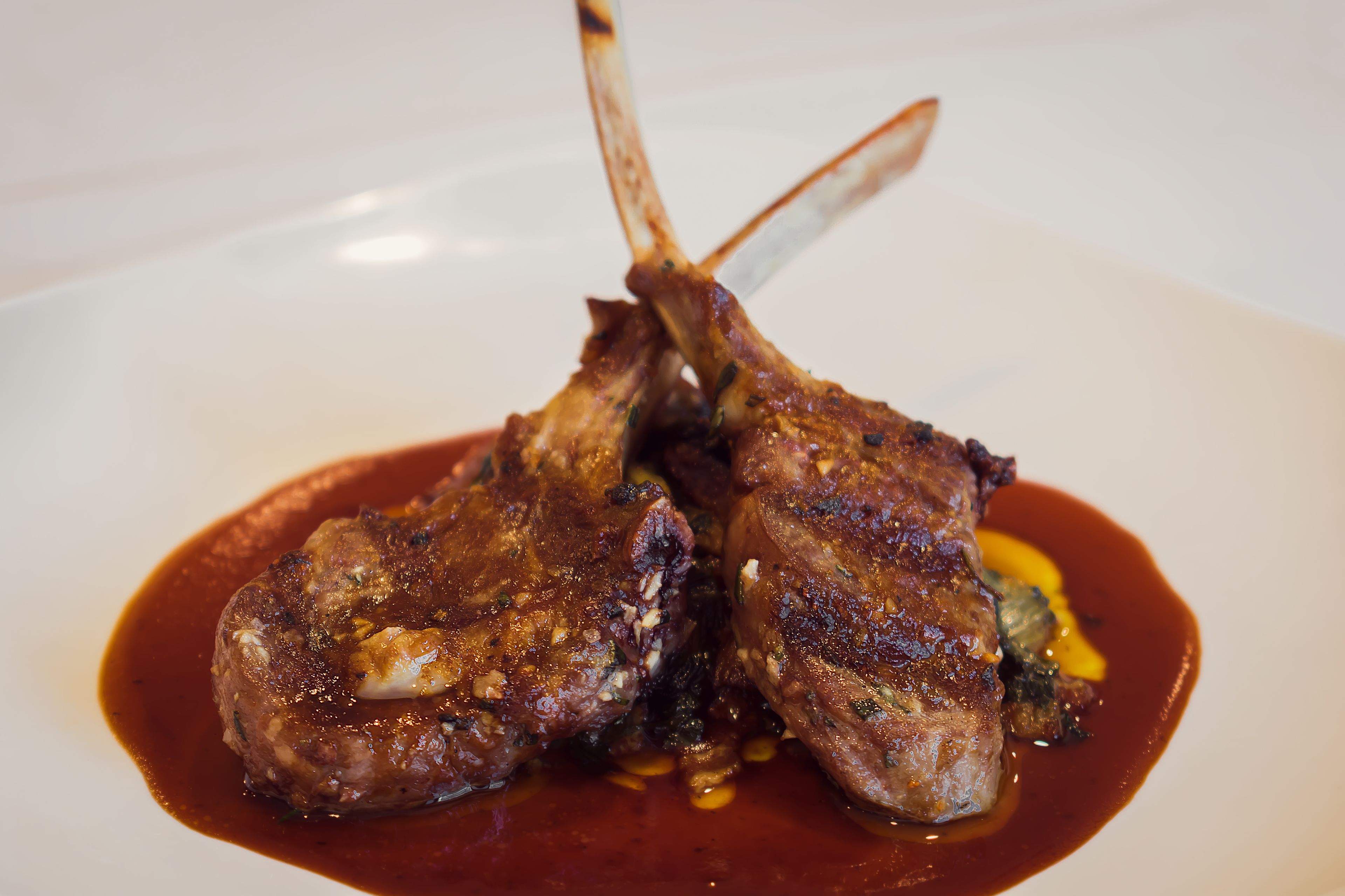 A plate with two lamb chops and a sauce.