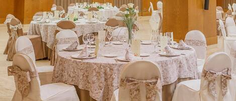 A banquet hall with round tables set for a formal event, featuring floral centerpieces and white tablecloths.