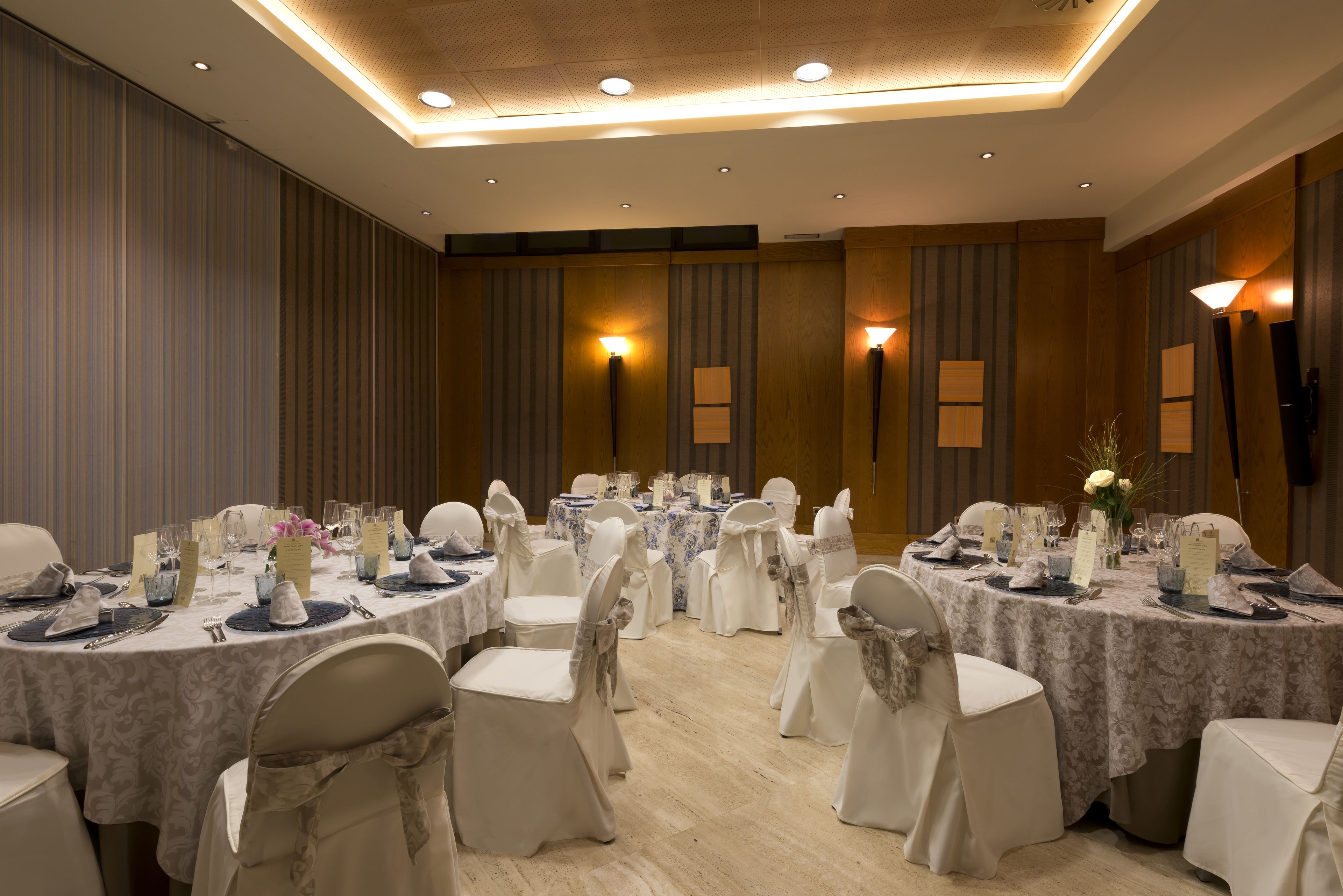 A banquet hall with round tables, white chairs, and chandeliers.