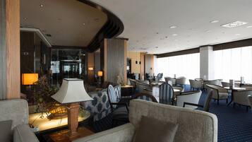 Un hall de hotel con áreas de descanso, una recepción y vistas al restaurante.