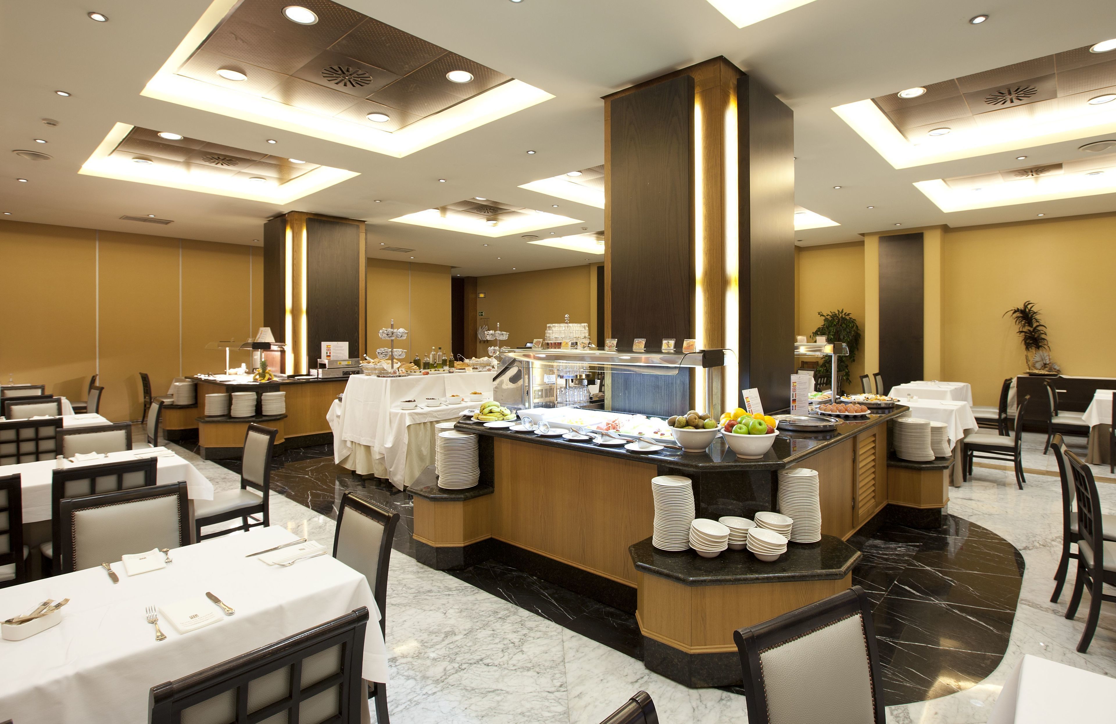 A hotel dining area with multiple tables, a buffet counter, and a central serving area.