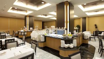 Un comedor de hotel con varias mesas, una barra de buffet y una zona central de servicio.