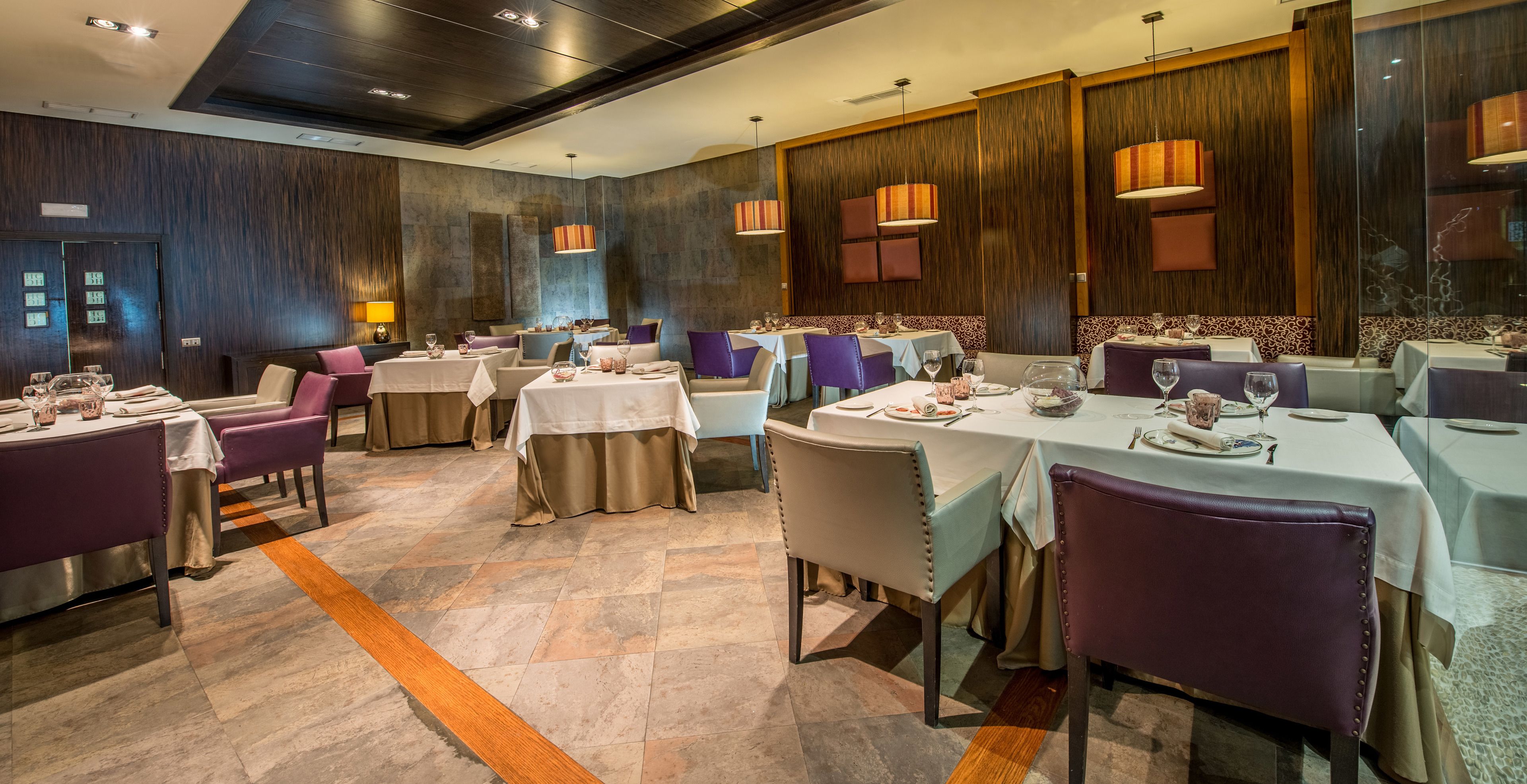 Um restaurante com várias mesas e cadeiras, paredes de painel de madeira e iluminação pendente.