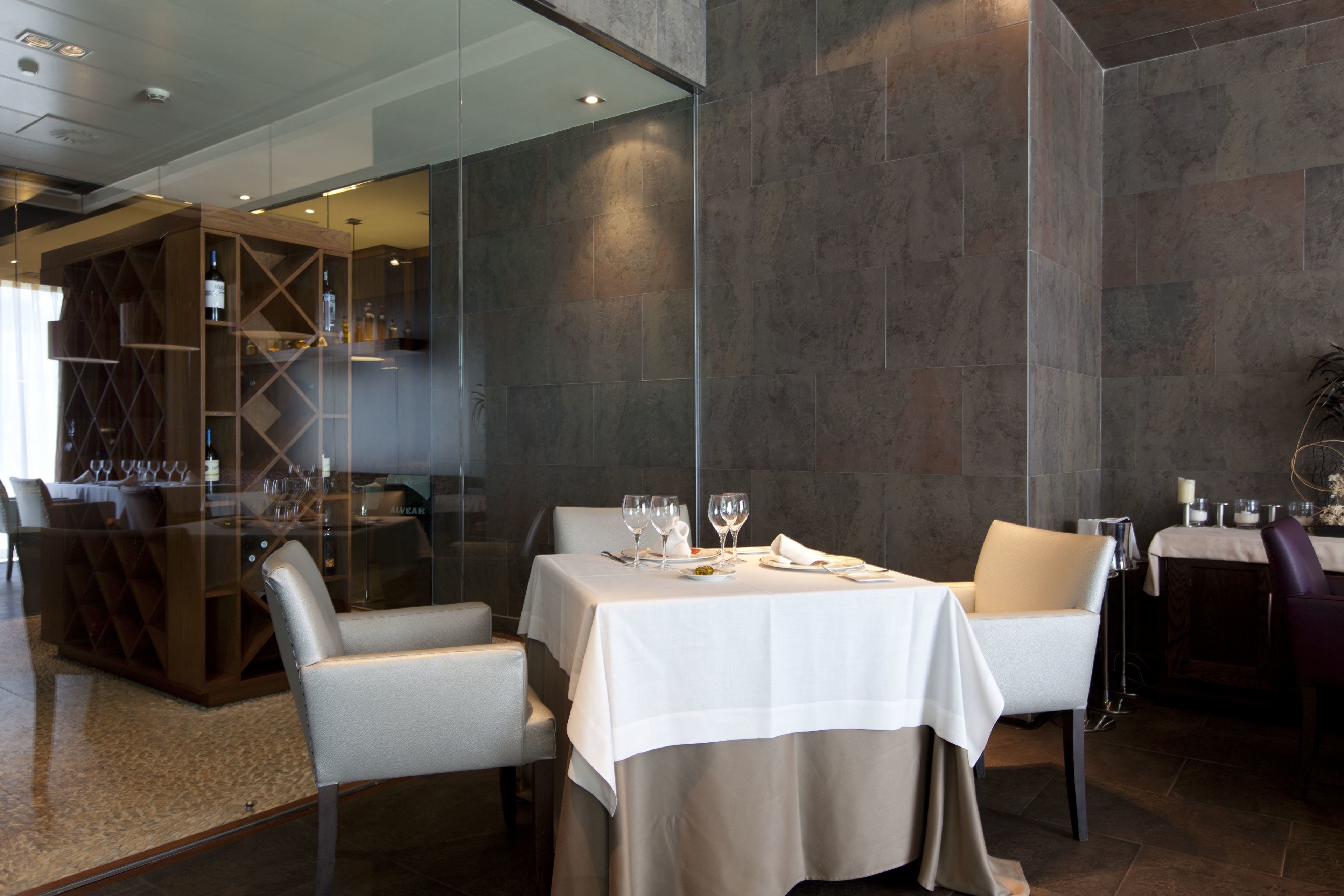 Un espace repas moderne avec une cloison en verre, des nappes blanches et un meuble à vin.