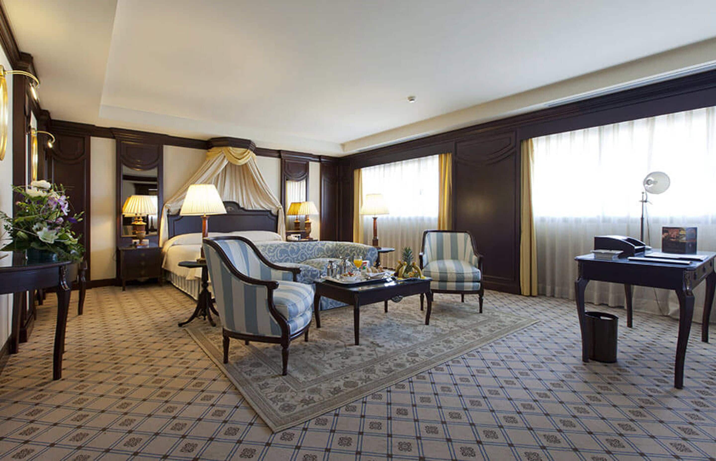 A hotel room with a bed, a sofa, a chair, a coffee table, a desk, and a lamp.