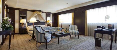 A hotel room with a bed, a sofa, a chair, a coffee table, a desk, and a lamp.