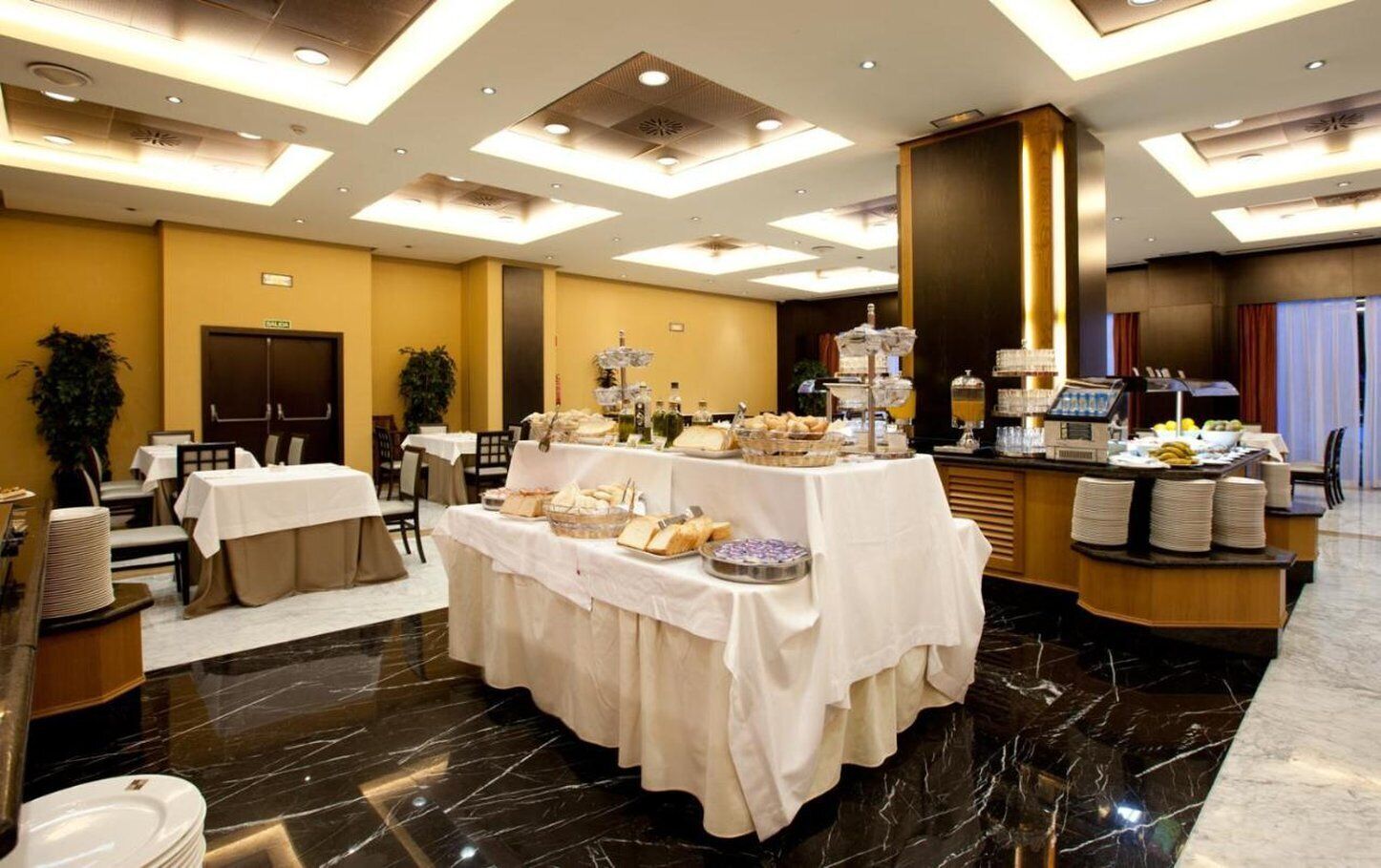 Un'area ristorazione in hotel con un buffet, tavoli, sedie e una reception.