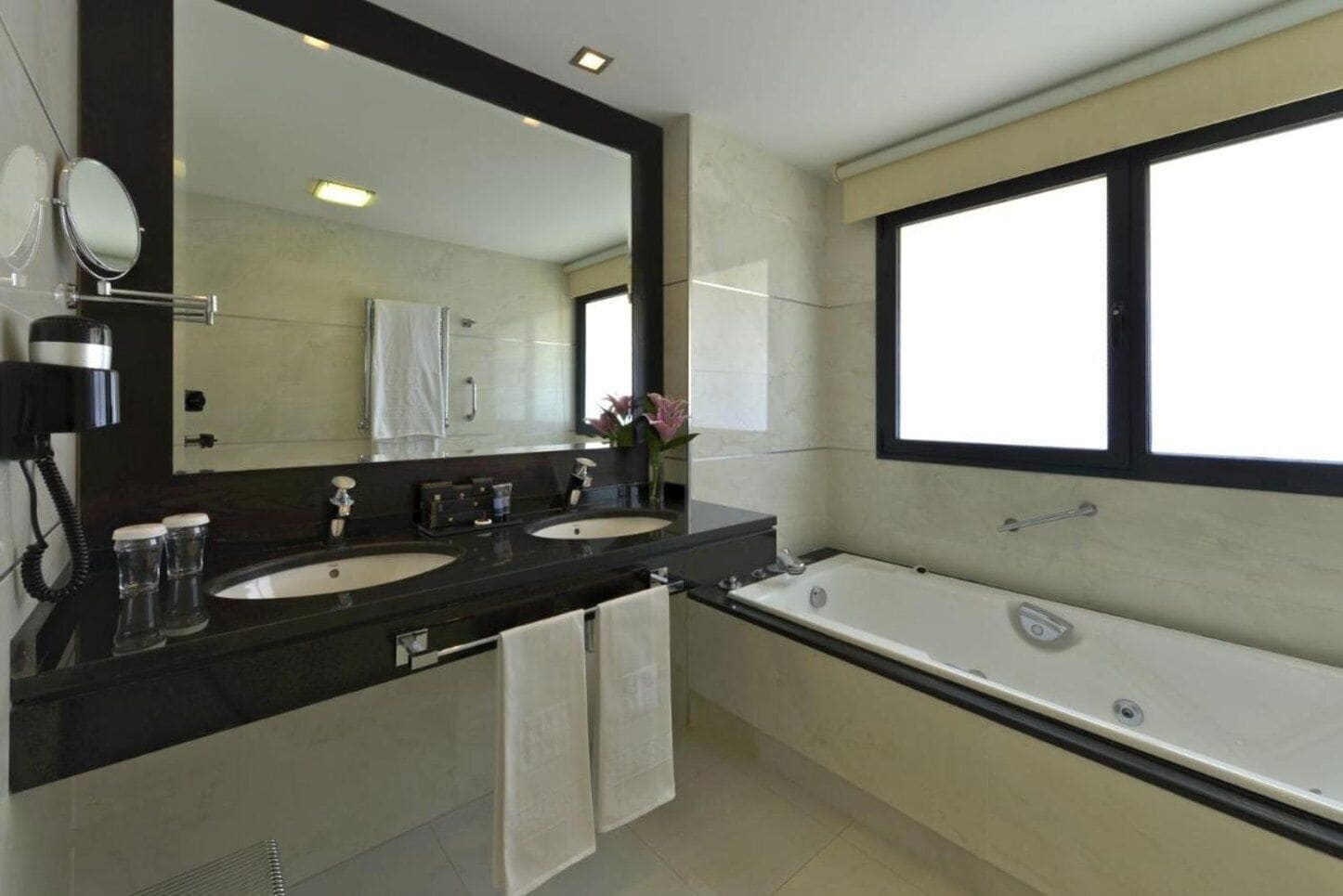 Un baño moderno con dos lavamanos, un espejo grande y una bañera.