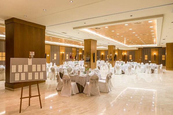 Un salón de banquetes con mesas redondas preparadas para un evento formal, destacando un caballete con papeles y un suelo de mármol pulido.