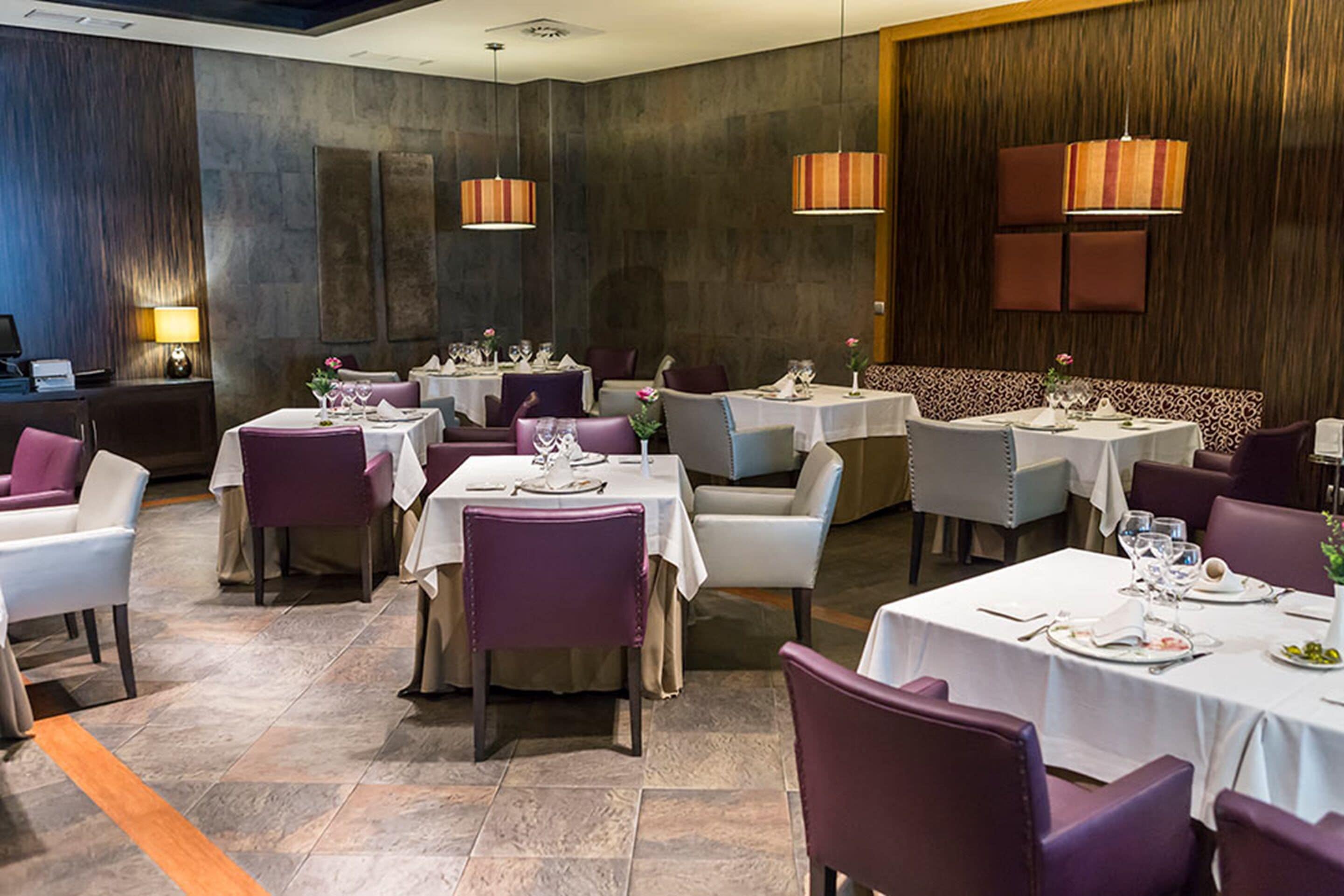 Een restaurant met meerdere tafels en stoelen, elk voorzien van een witte tafelkleed en paarse stoelen.