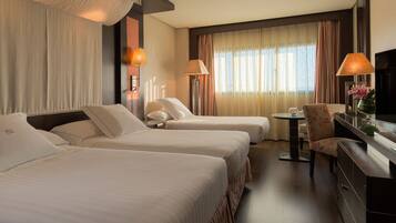 A hotel room with two beds, a desk, a chair, a TV, and a window with curtains.