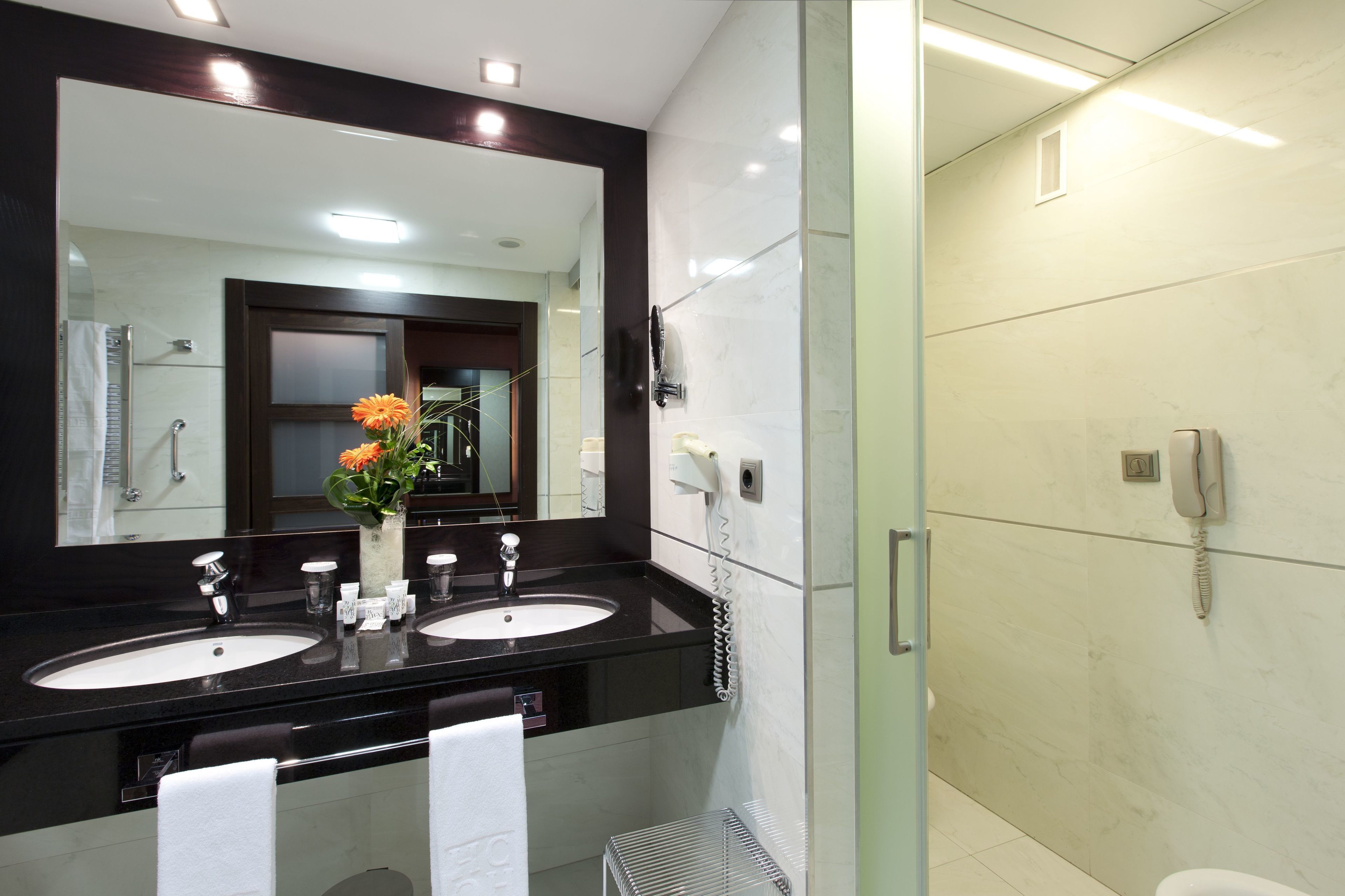 Une salle de bain moderne avec deux lavabos, un grand miroir et une douche à l’italienne.