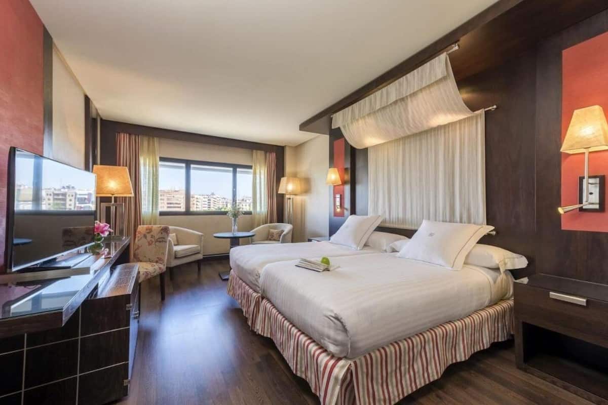 A hotel room with two beds, a TV, a desk, and a chair.
