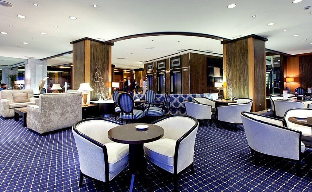 A modern hotel lobby with seating areas, a reception desk, and a patterned floor.