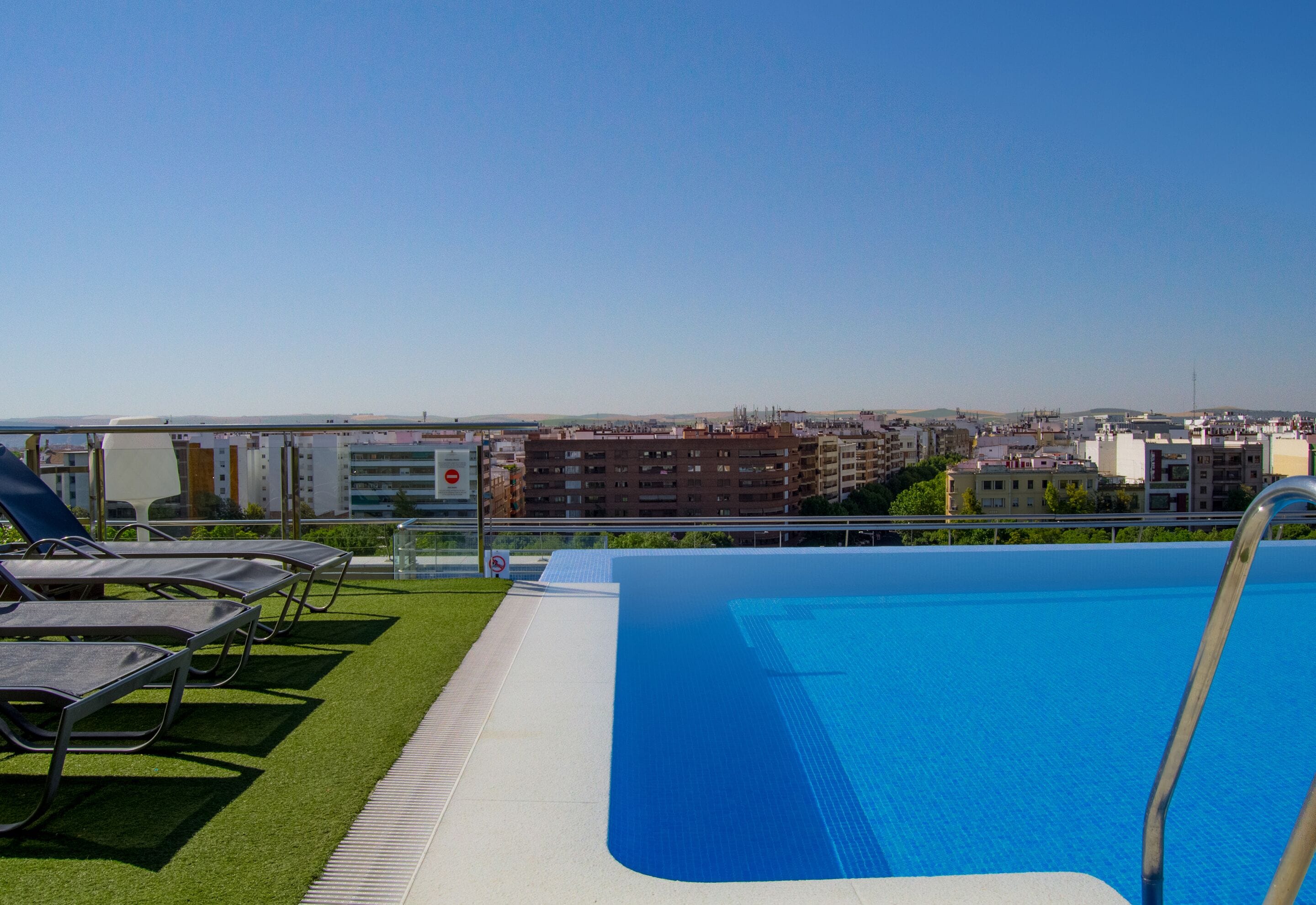 Una piscina en la azotea con sillones de descanso, vistas despejadas del paisaje urbano y un cartel de prohibido bañarse.