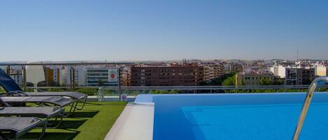 Una piscina en la azotea con sillones de descanso, vistas despejadas del paisaje urbano y un cartel de prohibido bañarse.