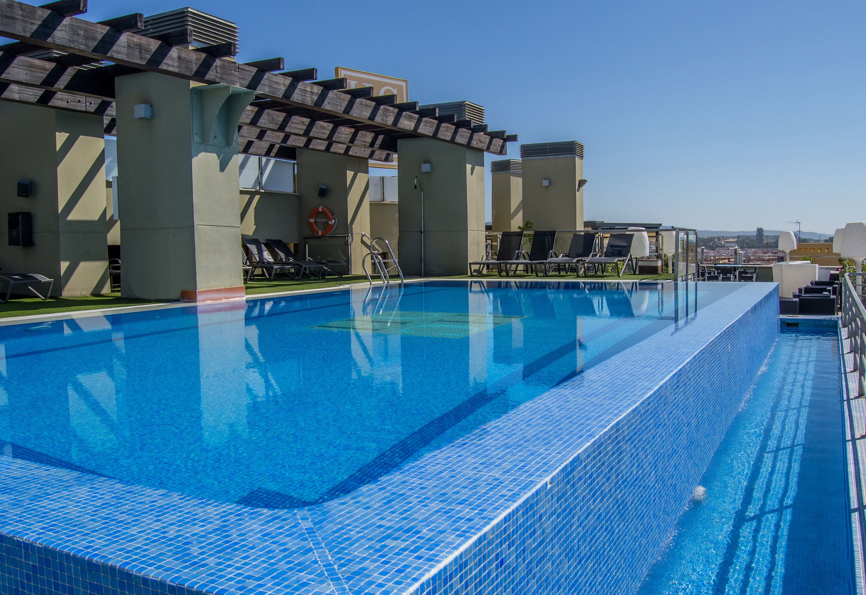A rooftop swimming pool with lounge chairs and a city view.