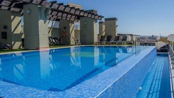 A rooftop swimming pool with lounge chairs and a city view.