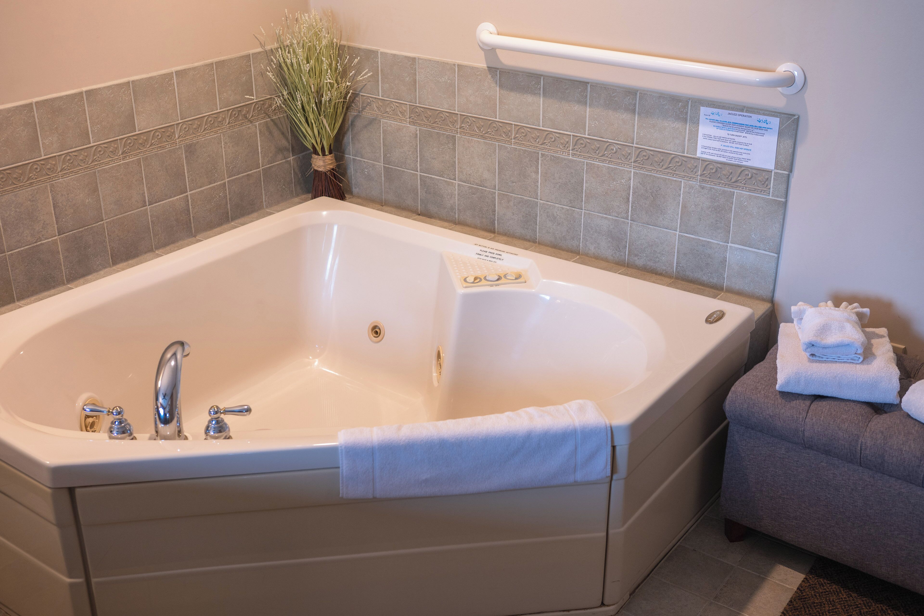 A large bathtub with a towel, a small stool, and a sign on the wall.