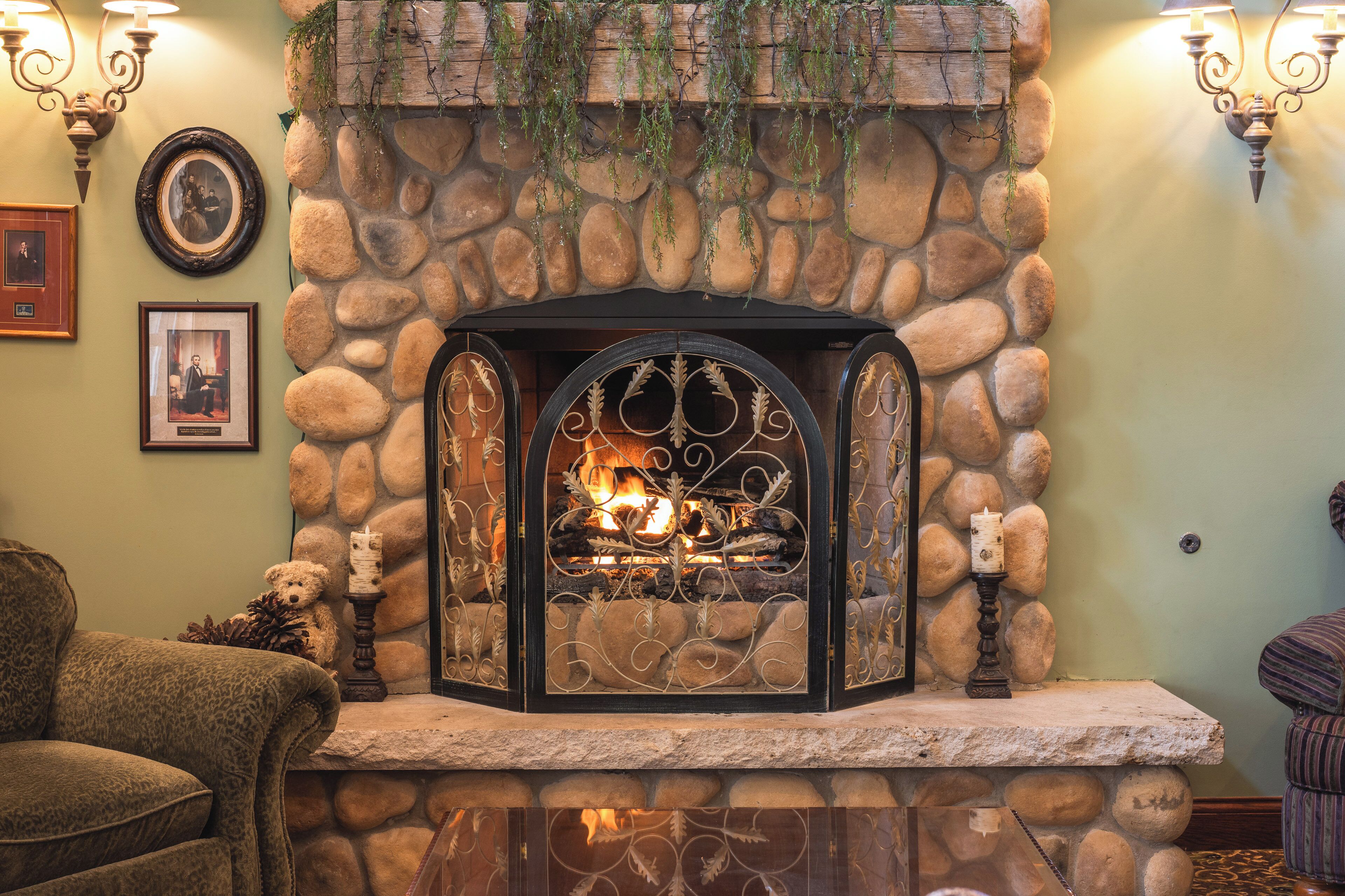 A stone fireplace with a fire, surrounded by a stone wall, with framed pictures and a bear statue on the mantel.